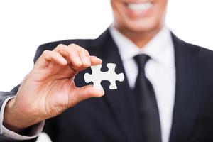 Providing support. Close-up of happy mature man in formalwear showing puzzle element and smiling while standing against white background photo