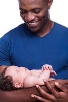 orgulloso de ser papá. primer plano de un joven africano feliz sosteniendo a su pequeño bebé y sonriendo mientras está de pie aislado en blanco foto