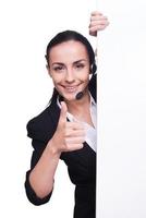 Providing only quality support. Beautiful young woman in headset standing near copy space and smiling while isolated on white photo