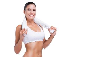 Relaxing after work out. Beautiful young woman in white bra and panties carrying towel on shoulders and smiling while standing isolated on white photo