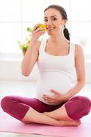 Only healthy eating for both of them. Beautiful pregnant woman sitting in lotus position and eating apple photo