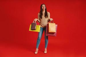 Full length of beautiful young woman in casual clothing carrying shopping bags and smiling photo