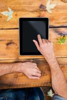 All the world in one touch. Close-up of man holding his finger on digital tablet while sitting at the wooden table outdoors photo