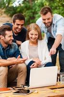 Sharing brilliant ideas. Group of cheerful young people looking at laptop while working together outdoors photo