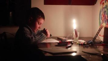 Boy draws a picture by candlelight. Turn off the electricity, global cataclysm video