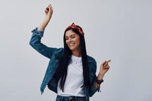 Attractive young woman in bandana smiling while dancing against grey background photo