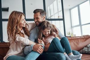 familia joven feliz sonriendo y abrazándose mientras se unen en casa foto