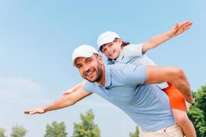 Piggyback ride. Smiling young man piggybacking his son while standing outdoors photo