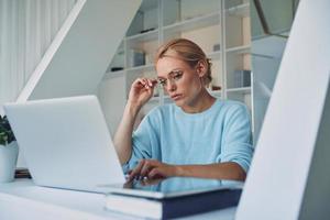 Beautiful young woman using laptop while working in office photo