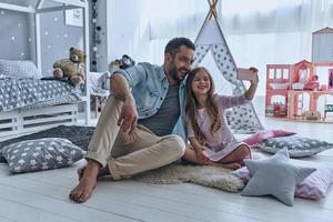 Selfie with dad. Young father and his little daughter taking selfie while sitting on the floor in bedroom with the tent in the background photo