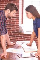 Business confrontation. Side view image of angry man and woman standing face to face while leaning at the office table photo