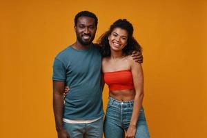 Beautiful young African couple looking at camera and smiling while standing against yellow background photo