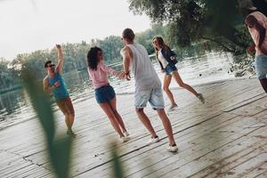 volviéndose loco. toda la longitud de los jóvenes en ropa casual sonriendo y divirtiéndose mientras están de pie en el muelle foto