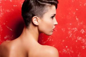 Beauty with stylish hairstyle. Rear view of beautiful young shirtless woman standing against red background photo