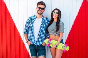 Funky couple. Cheerful young woman holding skateboard and bonding to her boyfriend while standing outdoors photo