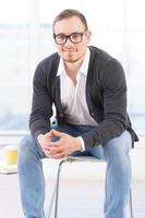 Looking for inspiration. Thoughtful young man in shirt looking at camera and smiling while sitting on the chair photo