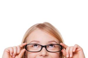 niña curiosa. imagen recortada de una niñita alegre que se ajusta las gafas y mira hacia arriba mientras está aislada en blanco foto