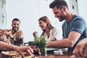 Buenos tiempos. grupo de jóvenes con ropa informal comiendo y sonriendo mientras cenan en el interior foto