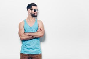 Young and carefree. Confident young handsome man in sunglasses keeping arms crossed and looking away with smile while standing against white background photo