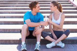 Exercising together is fun. Side view of beautiful young couple in sports clothing sitting on stairs face to face and smiling photo