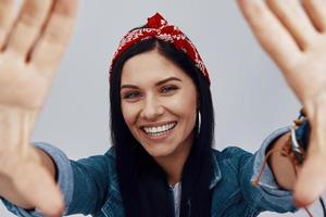 Atractiva mujer sonriente joven en bandana mirando a la cámara y haciendo marco de mano foto