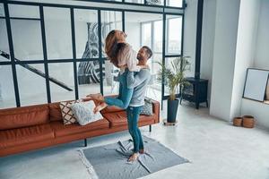 Full length of young happy couple smiling and dancing while bonding together at home photo