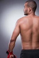 He is the best fighter. Rear view of shirtless African man in boxing gloves standing against grey background photo