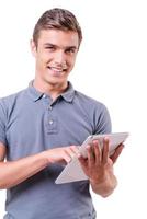 Examining his brand new gadget. Handsome young man working on digital tablet and smiling while standing isolated on white background photo