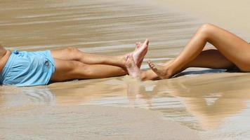två människor är Sammanträde på de sandig stranden. vågor tvätta över deras fötter. turism och resa begrepp video
