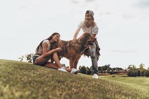 Enjoying time together. Young modern couple playing with their dog while spending free time in the park photo