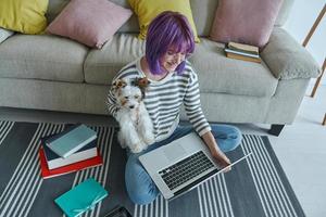 vista superior de una adolescente que lleva un lindo perrito mientras usa una laptop en casa foto