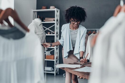 cada detalle debe ser perfecto. hermosa joven africana midiendo la cintura con cinta y anotando los resultados mientras está de pie en su taller foto