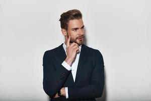 Thinking about... Handsome young man in formalwear looking away with smile while standing against grey background photo