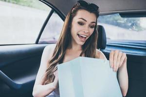What a beautiful dress Beautiful young smiling woman looking inside of the shopping bag and looking surprised while sitting inside of the car photo