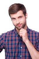 Thoughtful handsome. Portrait of thoughtful young man in casual shirt holding hand on chin and looking at camera while standing isolated on white photo