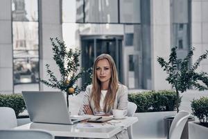 Busy working day. Beautiful young woman looking at camera while sitting in the modern restaurant photo