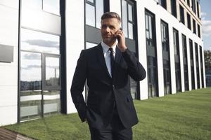Confident mature businessman talking on mobile phone while standing near office building photo