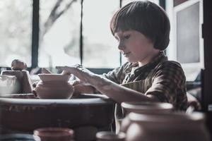 He loves pottering. Confident little boy making ceramic pot on the pottery class photo