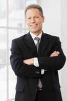 Confident businessman. Cheerful mature man in formalwear smiling at camera while standing near window photo