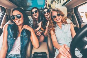 solo camino por delante cuatro hermosas mujeres jóvenes y alegres mirando la cámara con una sonrisa mientras están sentadas en el auto foto