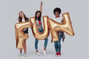 longitud total de tres mujeres jóvenes atractivas que llevan globos y sonríen mientras están de pie contra el fondo gris foto