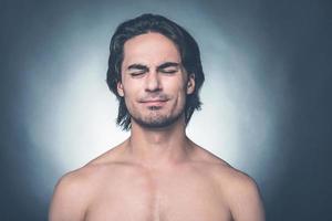 Feeling not good. Portrait of young shirtless man keeping eyes closed and expressing negativity while standing against grey background photo