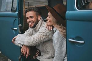 Enjoying every minute together.  Beautiful young woman looking at her boyfriend and smiling while sitting in blue retro style mini van
