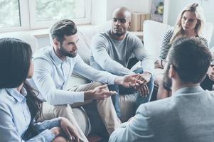 Sharing his problems with group. Group of young people sitting in circle while one man telling something and gesturing photo