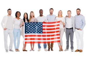 Team of America. Full length of happy diverse group of people bonding to each other and holding flag of America while standing against white background together photo