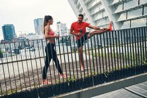 Full length of fit young couple in sports clothing warming up and stretching while practicing outdoors on the city street photo