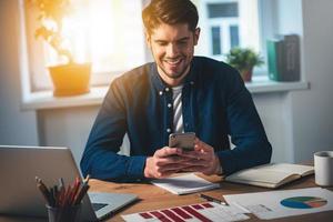 You have new message Cheerful young handsome man using his smartphone with smile while sitting at his working place photo