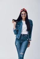 Attractive young woman in eyewear and bandana smiling while standing against grey background photo