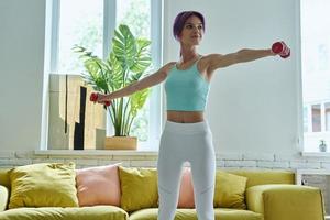 mujer joven confiada en ropa deportiva haciendo ejercicio con pesas en casa foto