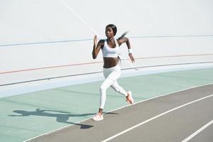 Beautiful young African woman in sports clothing running on track outdoors photo